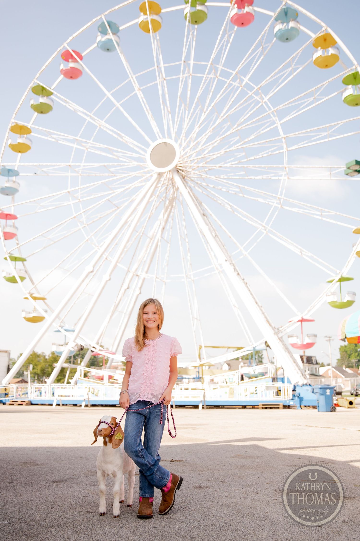 A person poses with a light-colored dog in front of a colorful ferris wheel at a carnival.