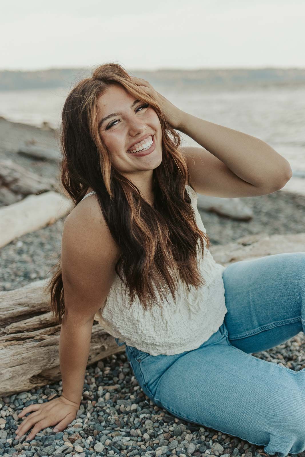 Brown hairded girl sitting on a beach with a big smile