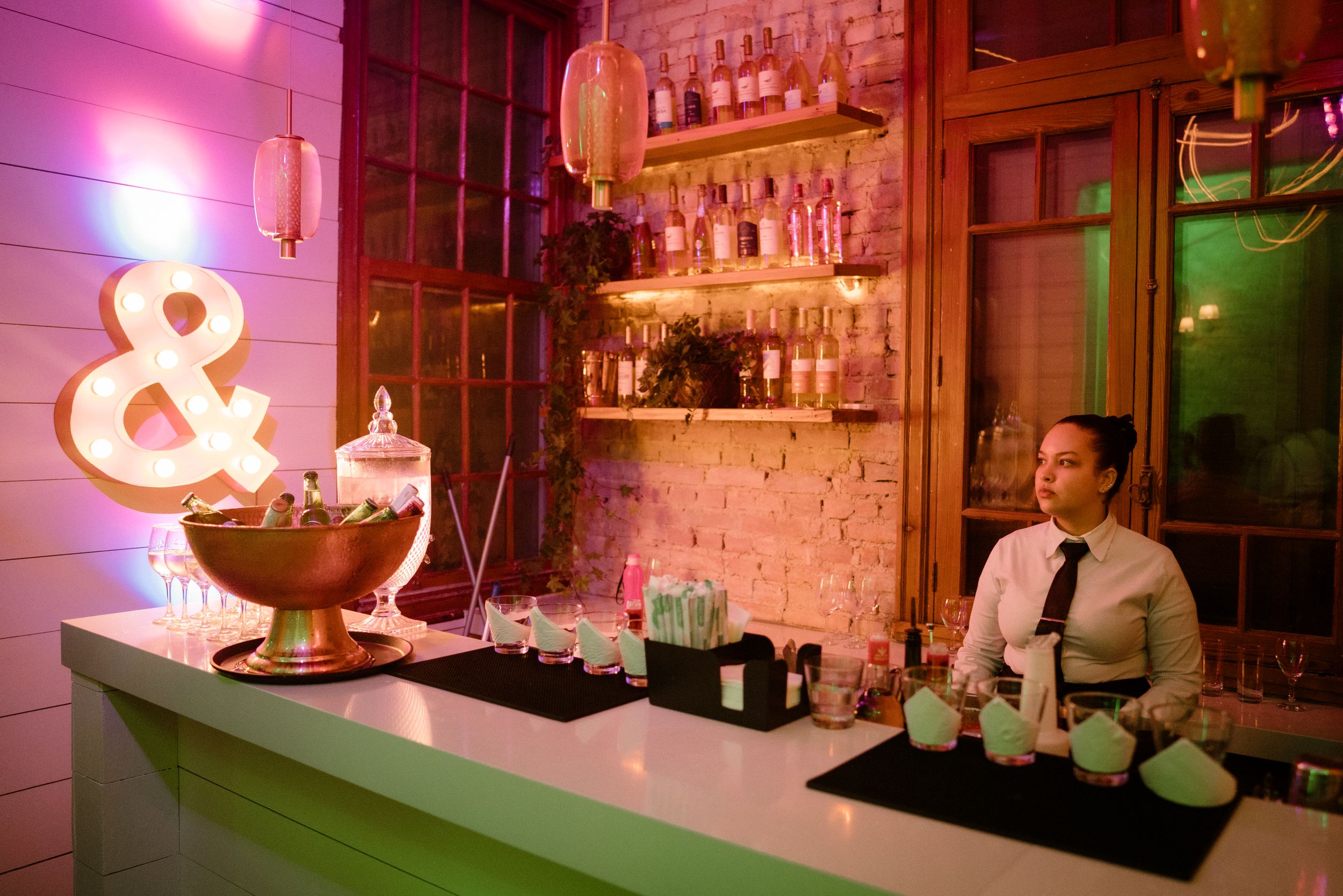 Pink-lit bar area with illuminated ampersand sign and exposed brick wall.