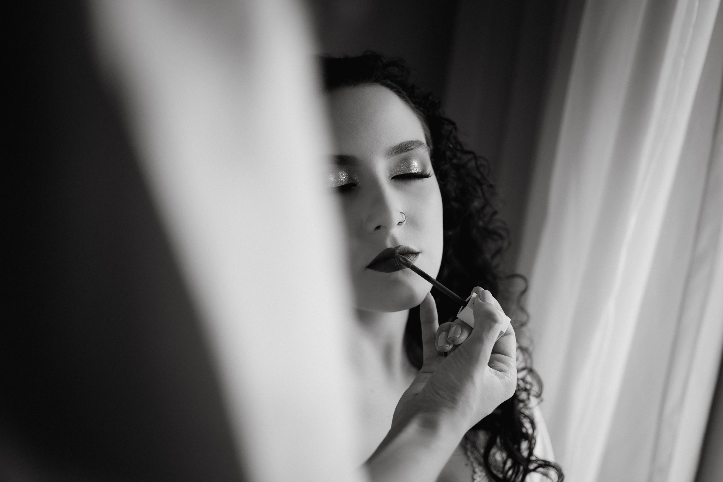 Black and white photo of makeup being applied to woman with dark curly hair.
