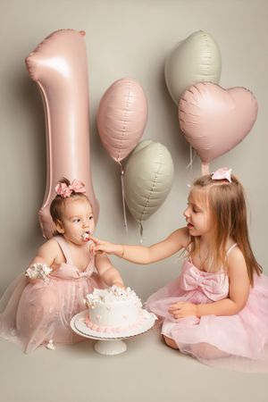 first birthday cake smash photography with pink balloons and sisters