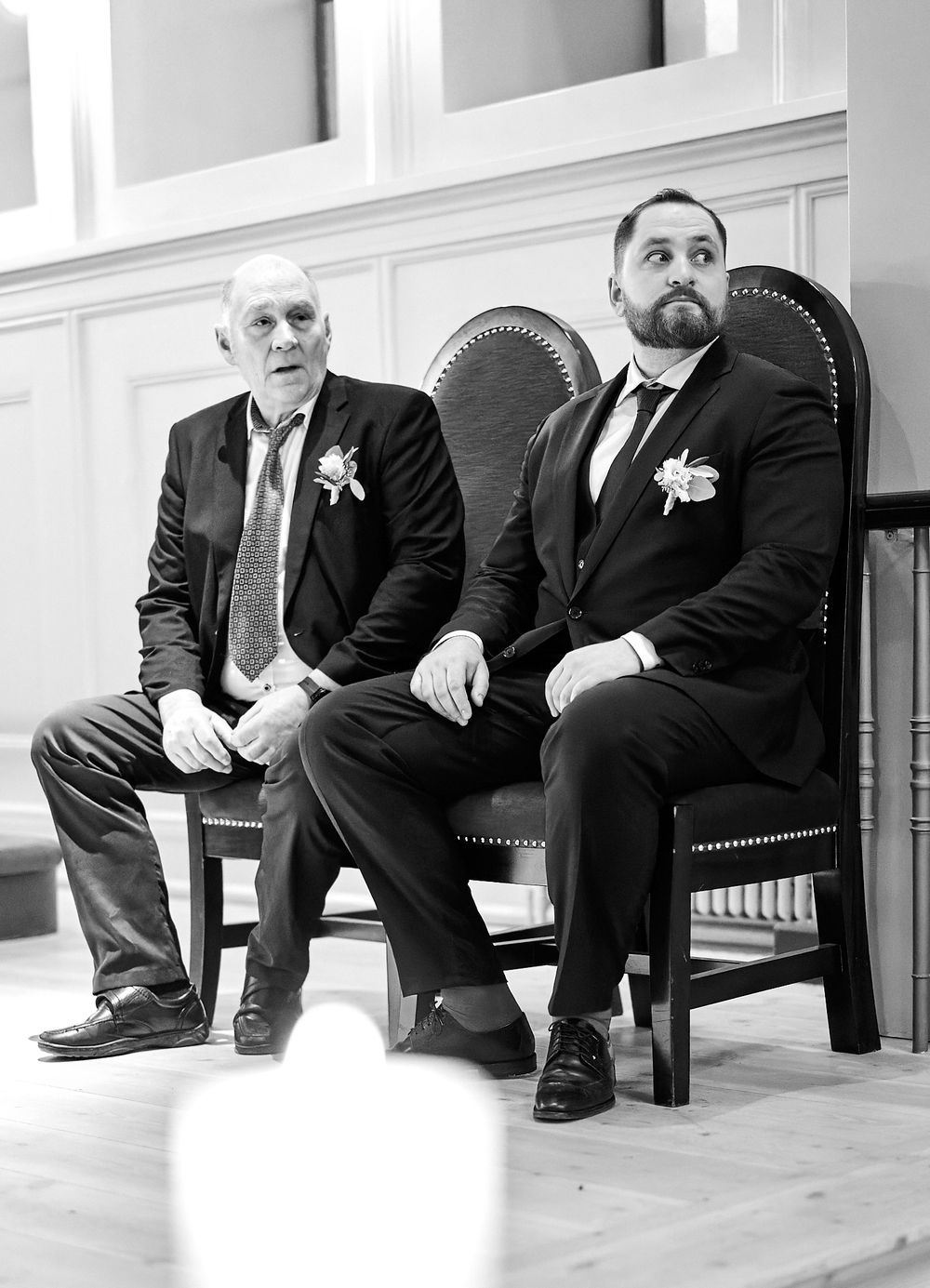 A black and white photo of two men seated in ornate chairs inside a church.