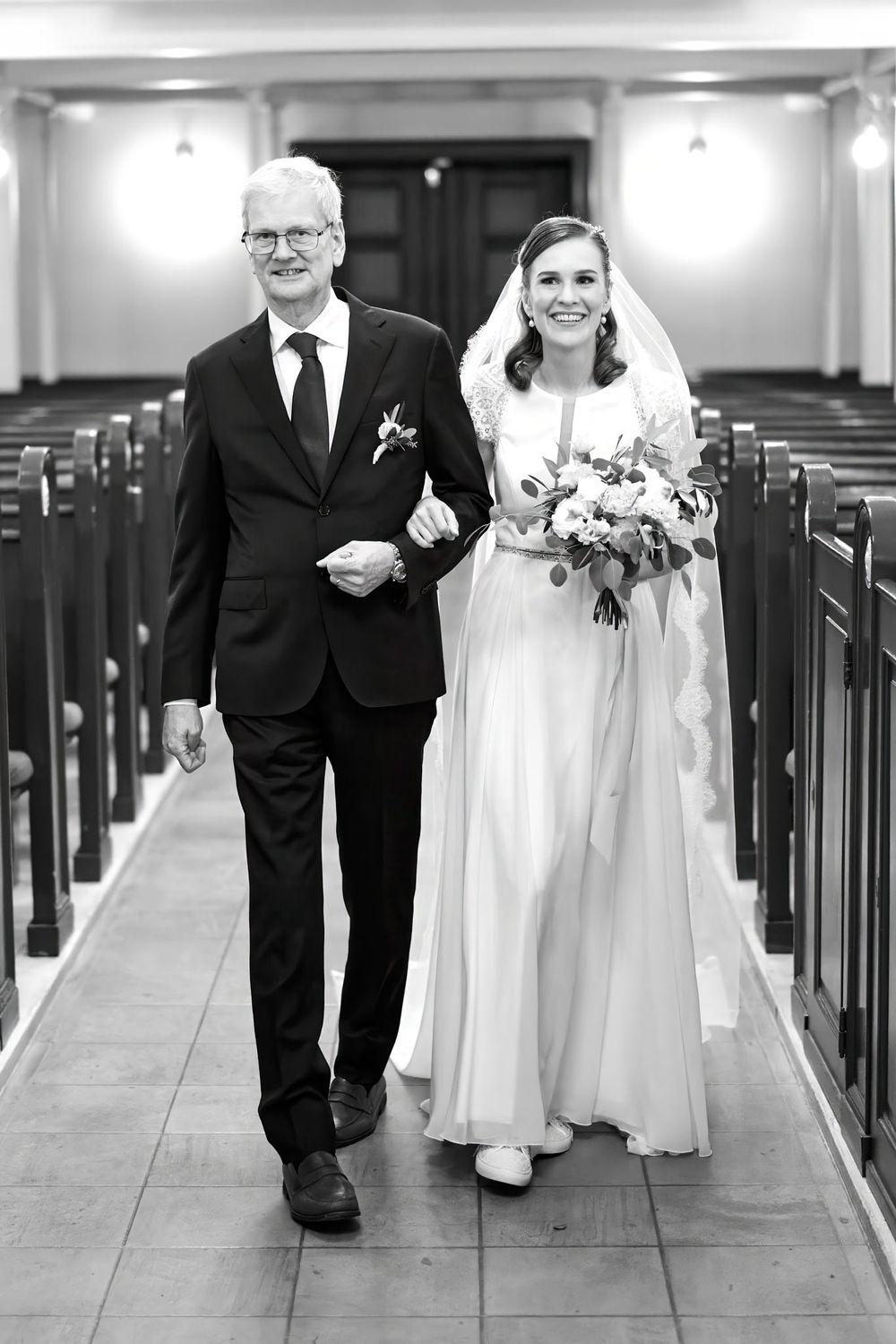 Black and white photo of wedding processional in church with wooden pews.