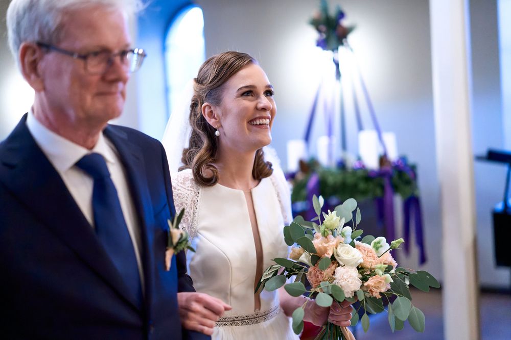 A bride in a white dress carries a pink and white bouquet during her wedding ceremony.