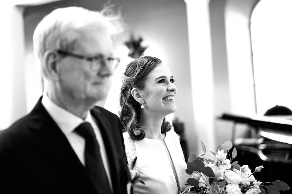 Black and white photo of a bride with upswept hair smiling during her wedding ceremony.