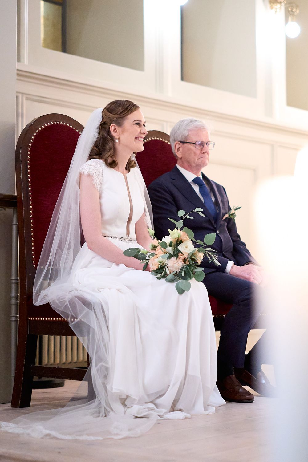 Wedding scene with decorated interior featuring red velvet chair and formal attire.