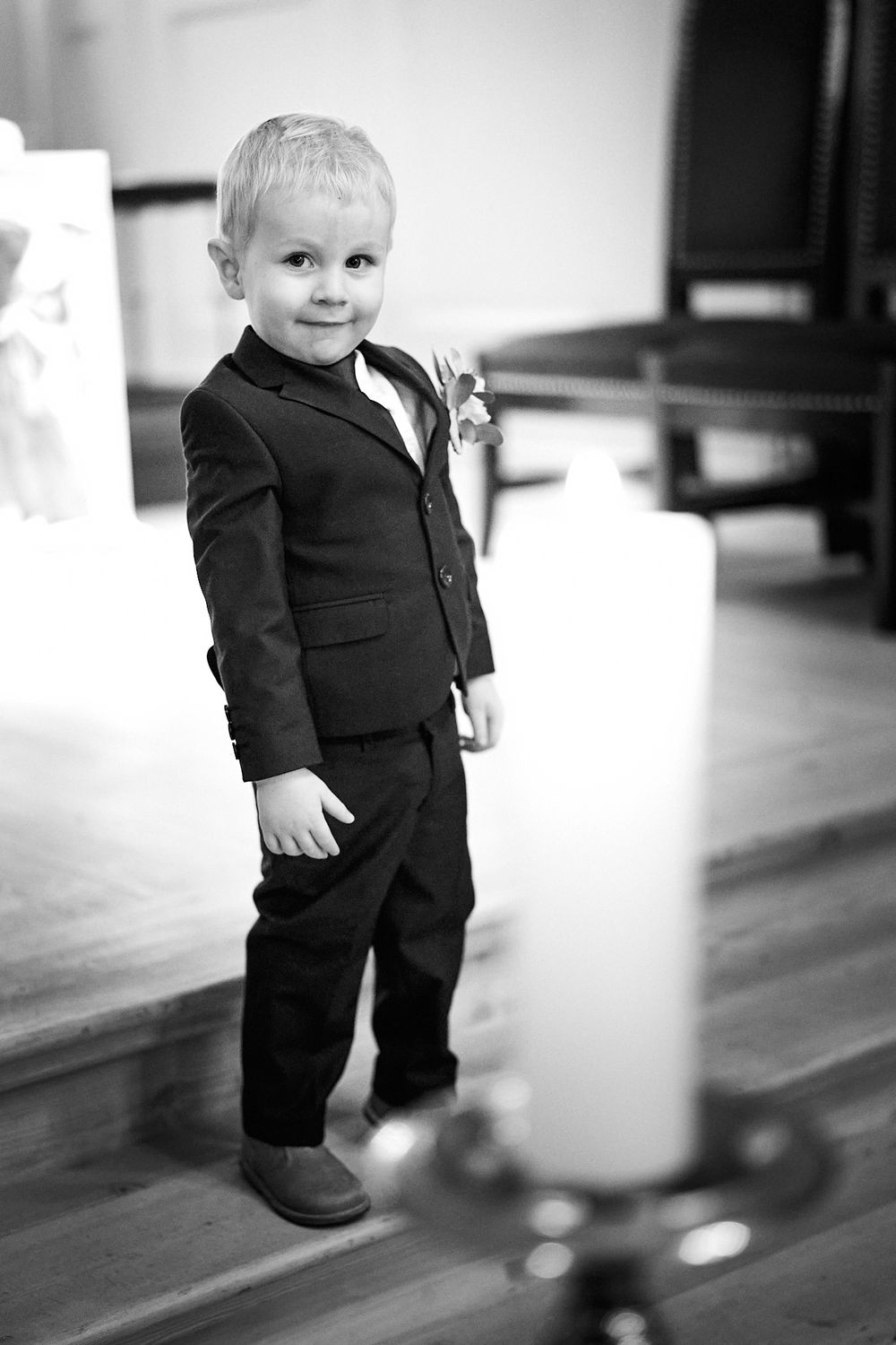 Black and white portrait of a young ring bearer in a formal suit at a wedding ceremony.