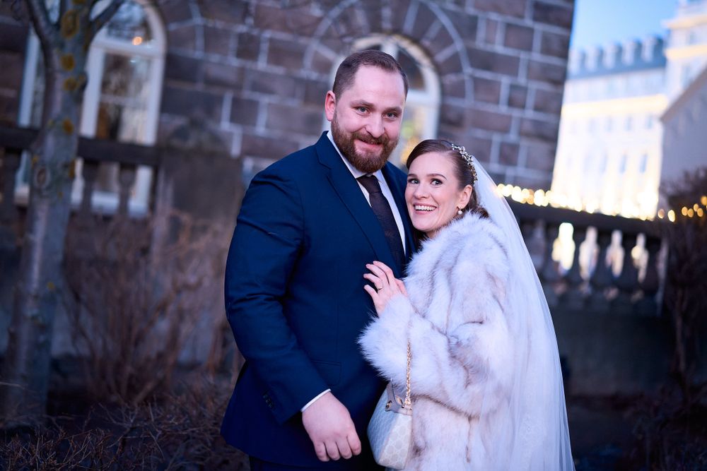 Wedding couple in winter attire pose together against brick church exterior.