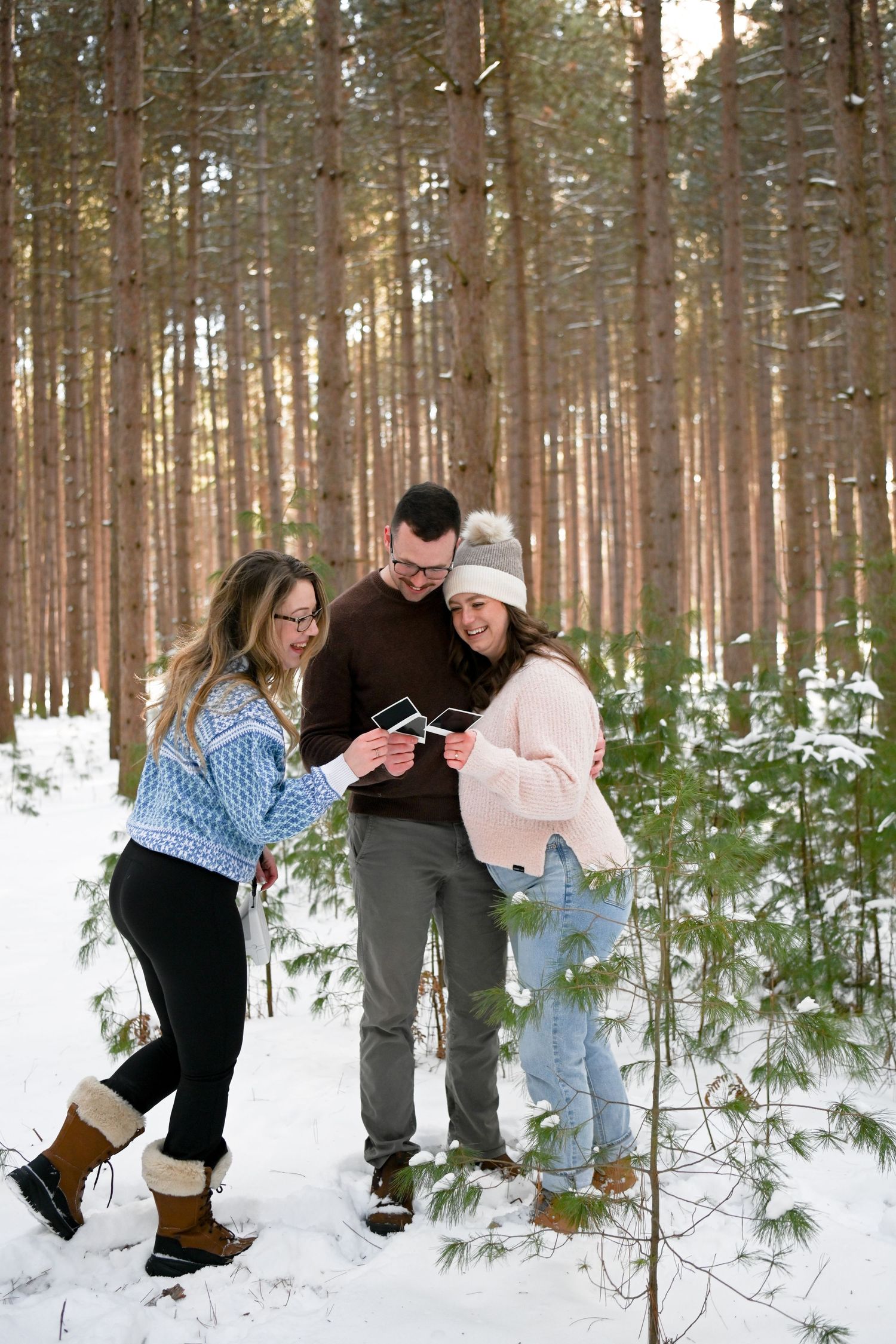 Three friends looking at photos together in a snowy winter forest.