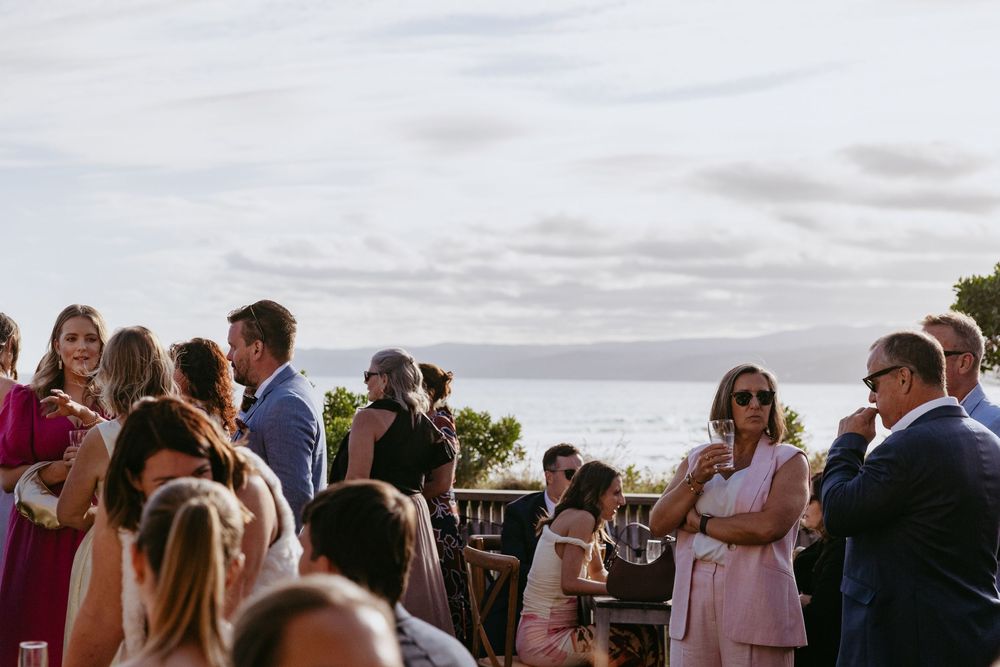 Wedding guests gather outdoors at a scenic venue during sunset, creating a lively social atmosphere.