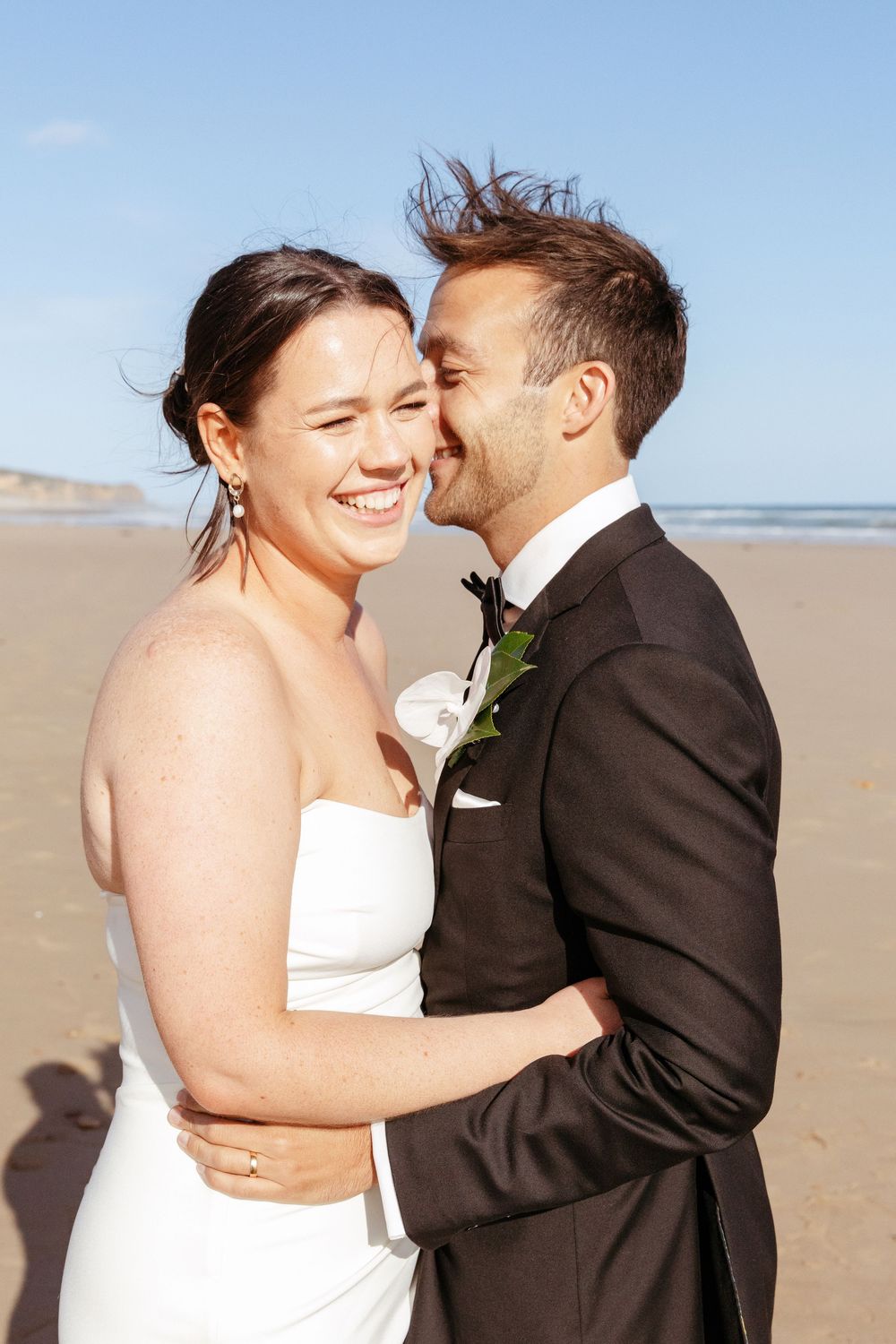 A couple shares a romantic moment on a sunny beach during their wedding photoshoot.
