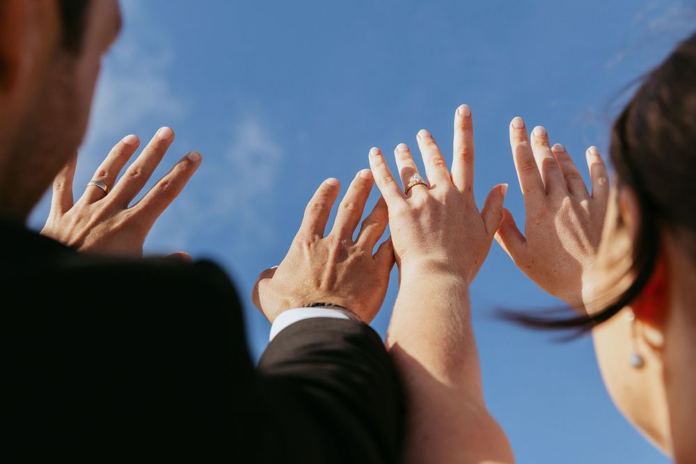 Silhouetted hands raised against a bright blue sky in a celebratory gesture.