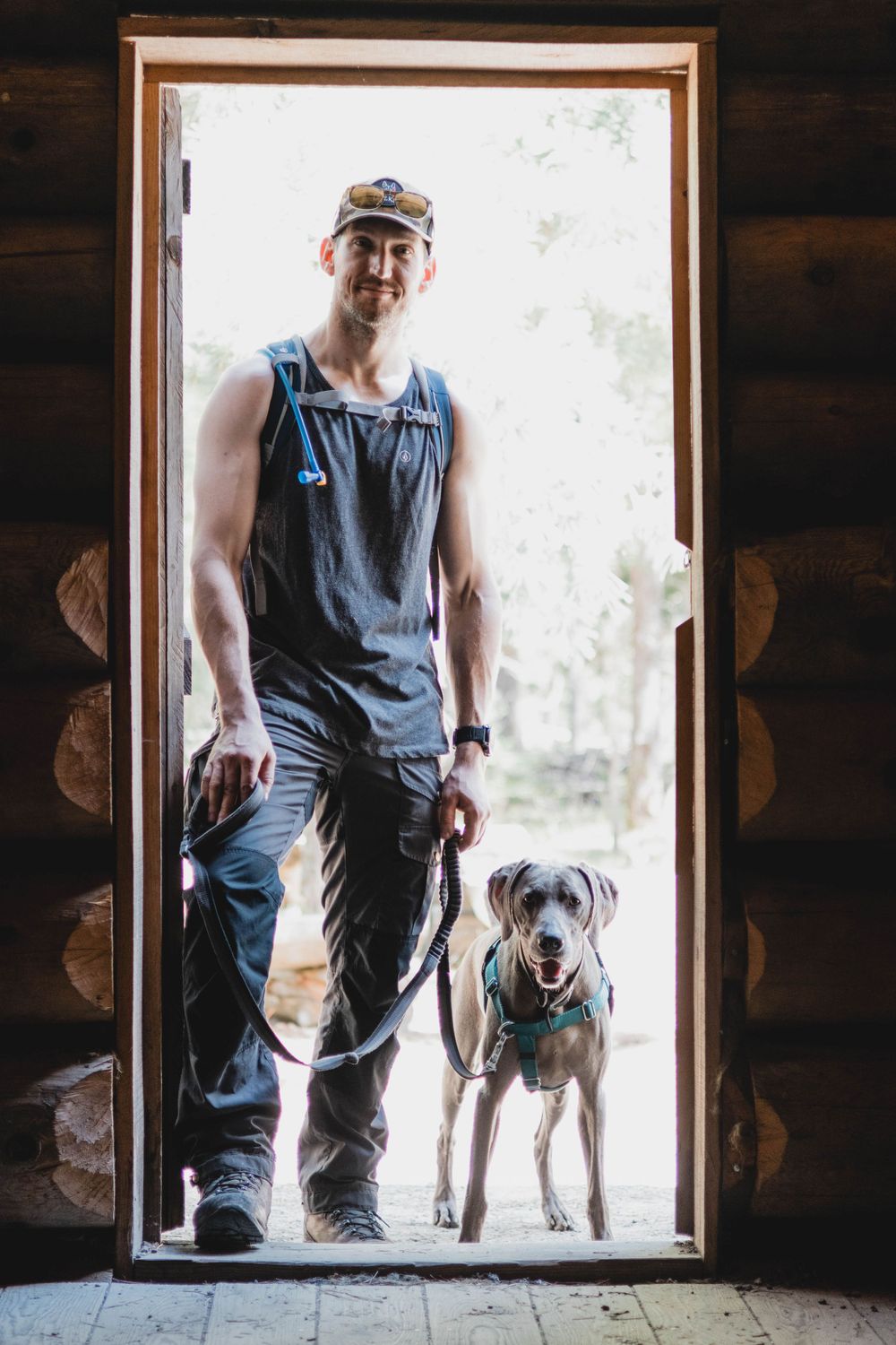 A dog and their companion stand silhouetted in a rustic cabin doorway.