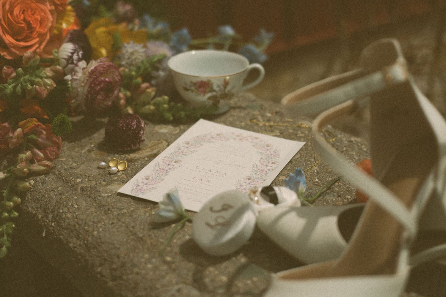 Wedding details with invitation, teacup, and decorative elements arranged on textured surface.