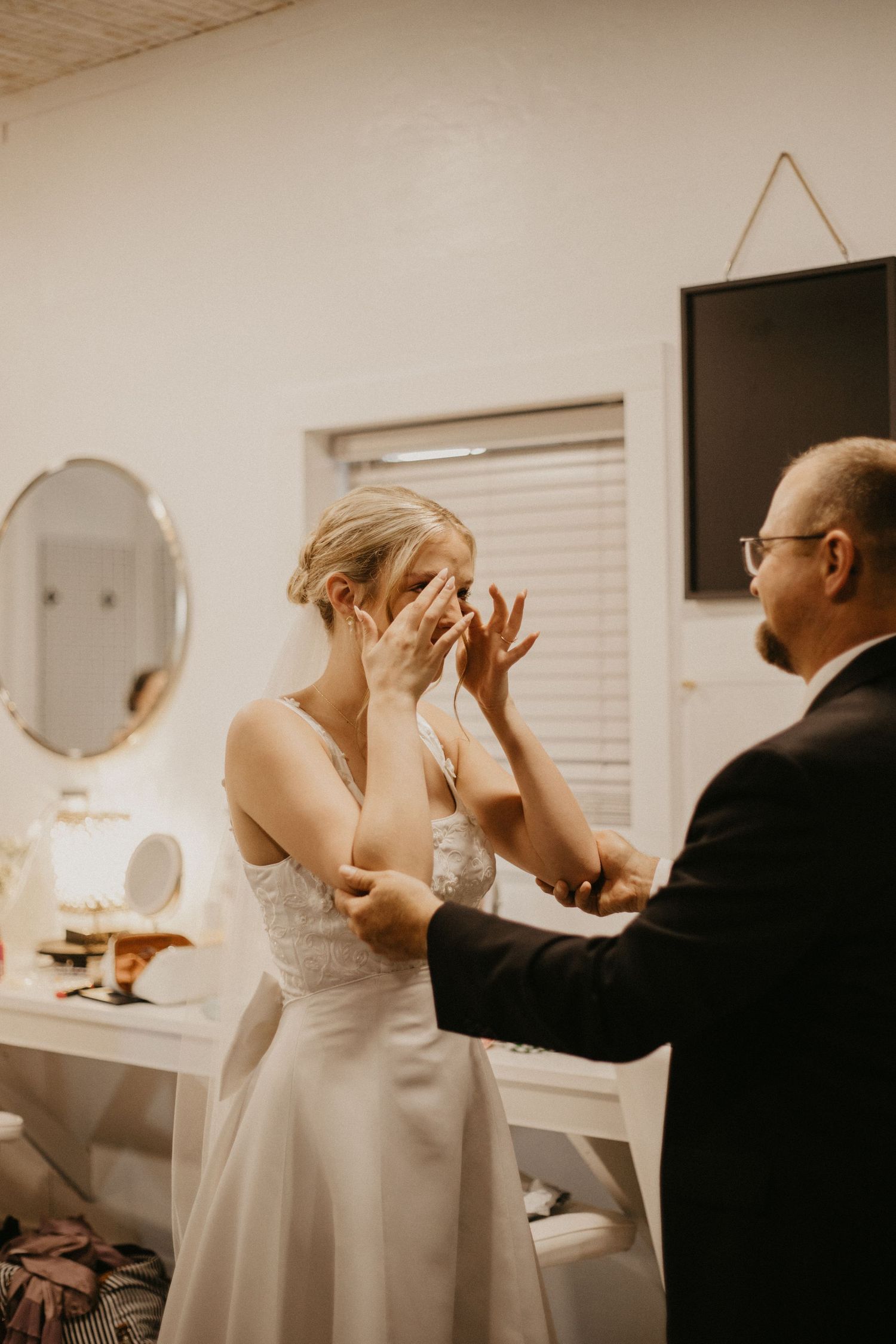 Emotional moment captured in getting ready room with figure in white wedding dress.