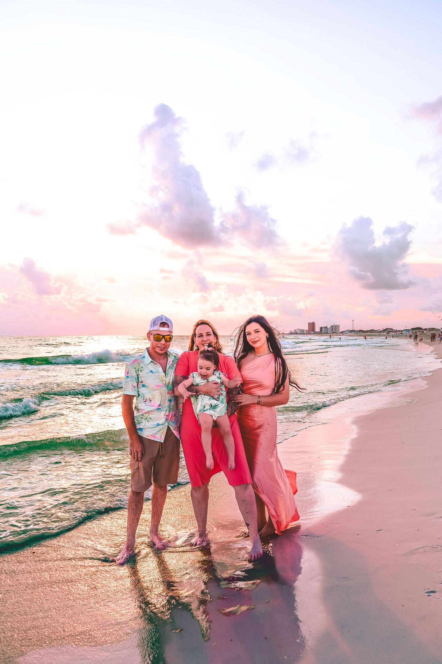A group enjoying a sunset stroll along a beach with pink and purple skies and rolling waves in the background.