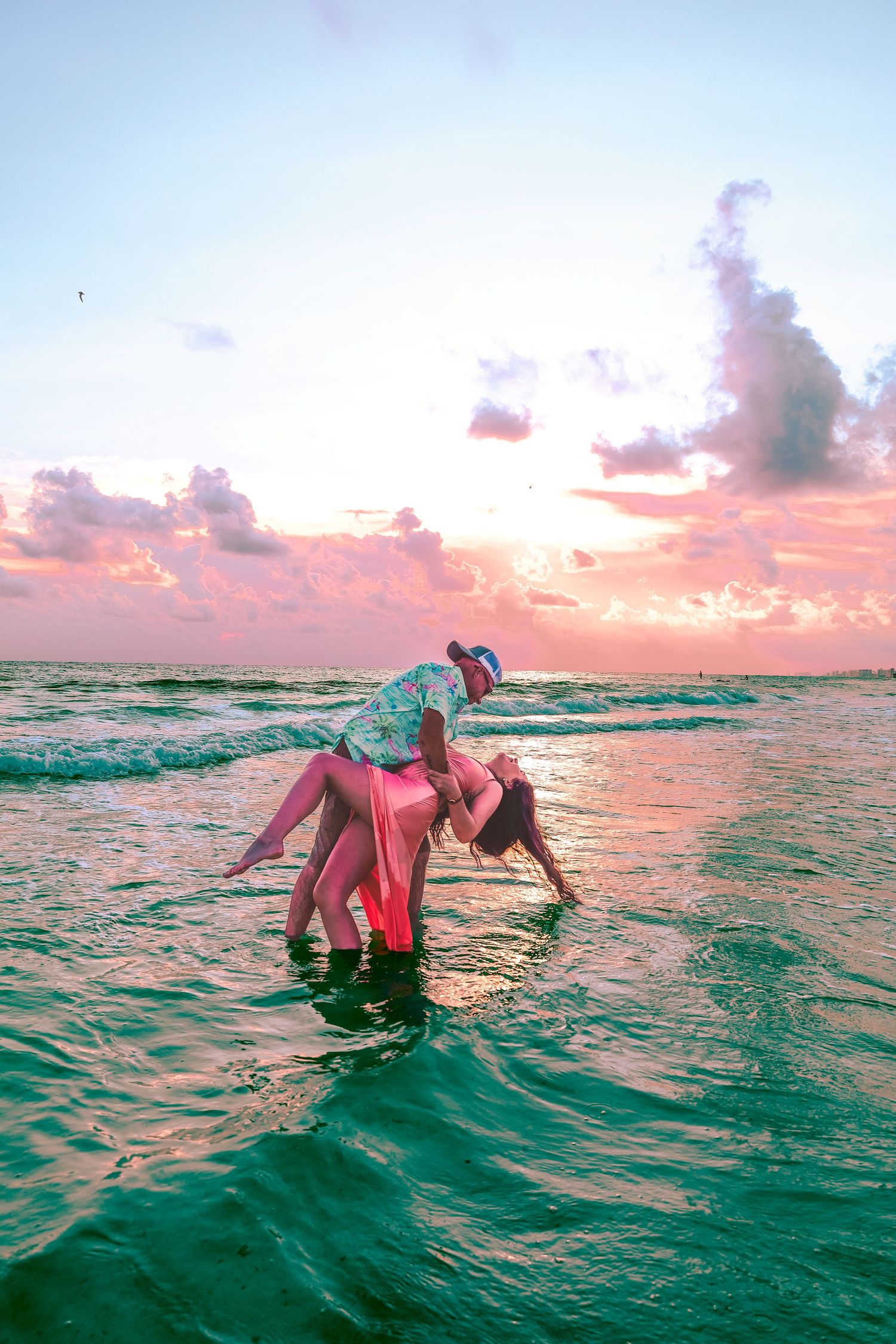 A person floats gracefully in turquoise ocean waters during a vibrant pink and orange sunset.