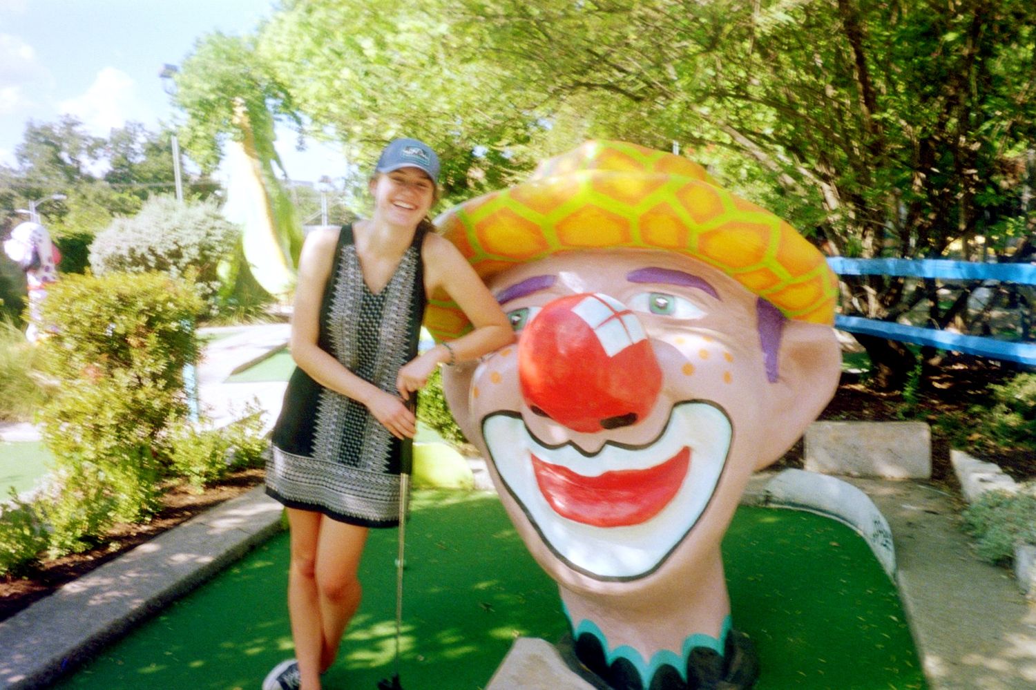 A person posing with a large colorful clown head at the Peter Pan mini golf course in Austin, TX.
