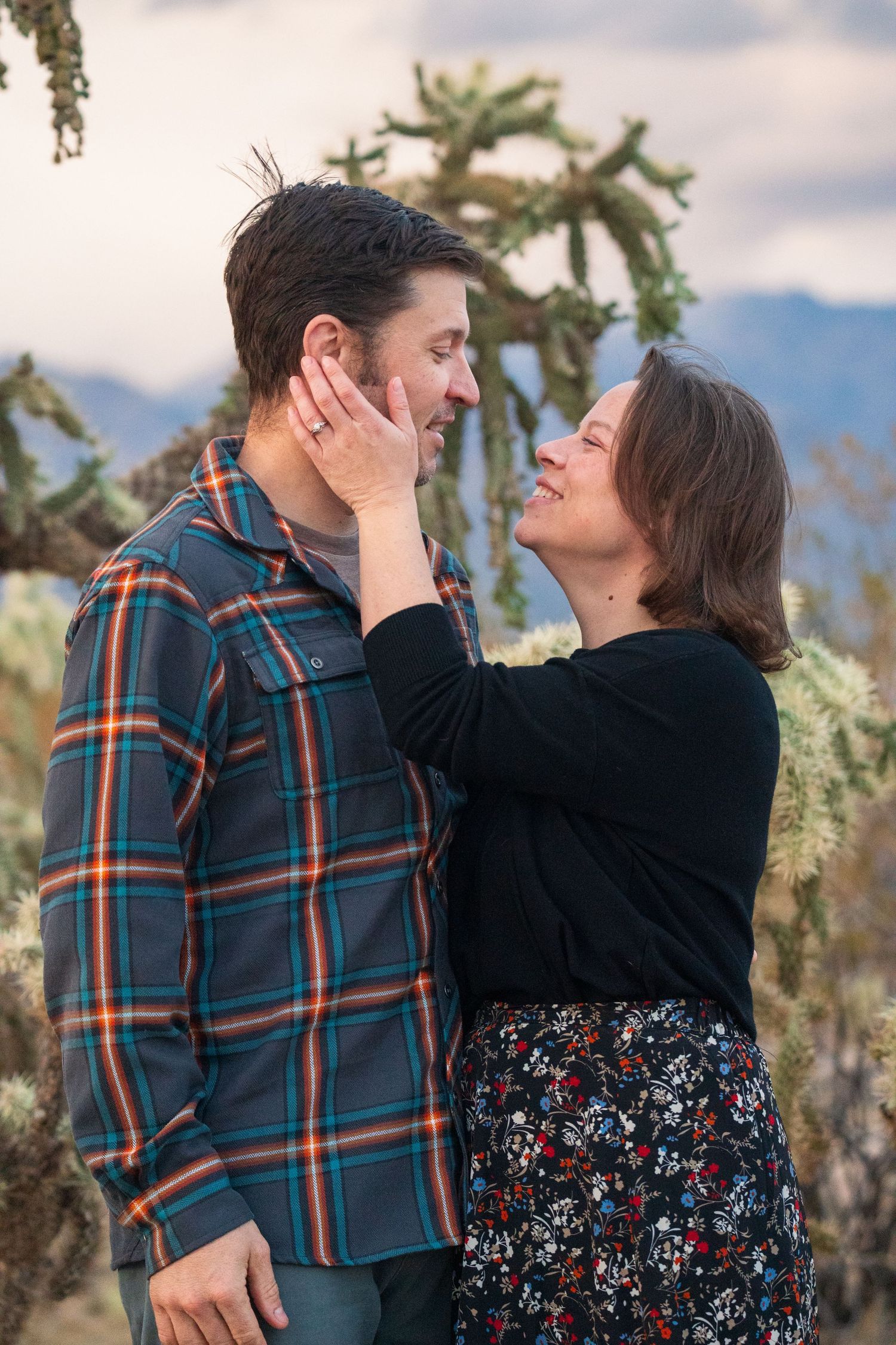 A tender moment between a couple against a mountain landscape with desert plants. Arizona desert photography adventure engagement session