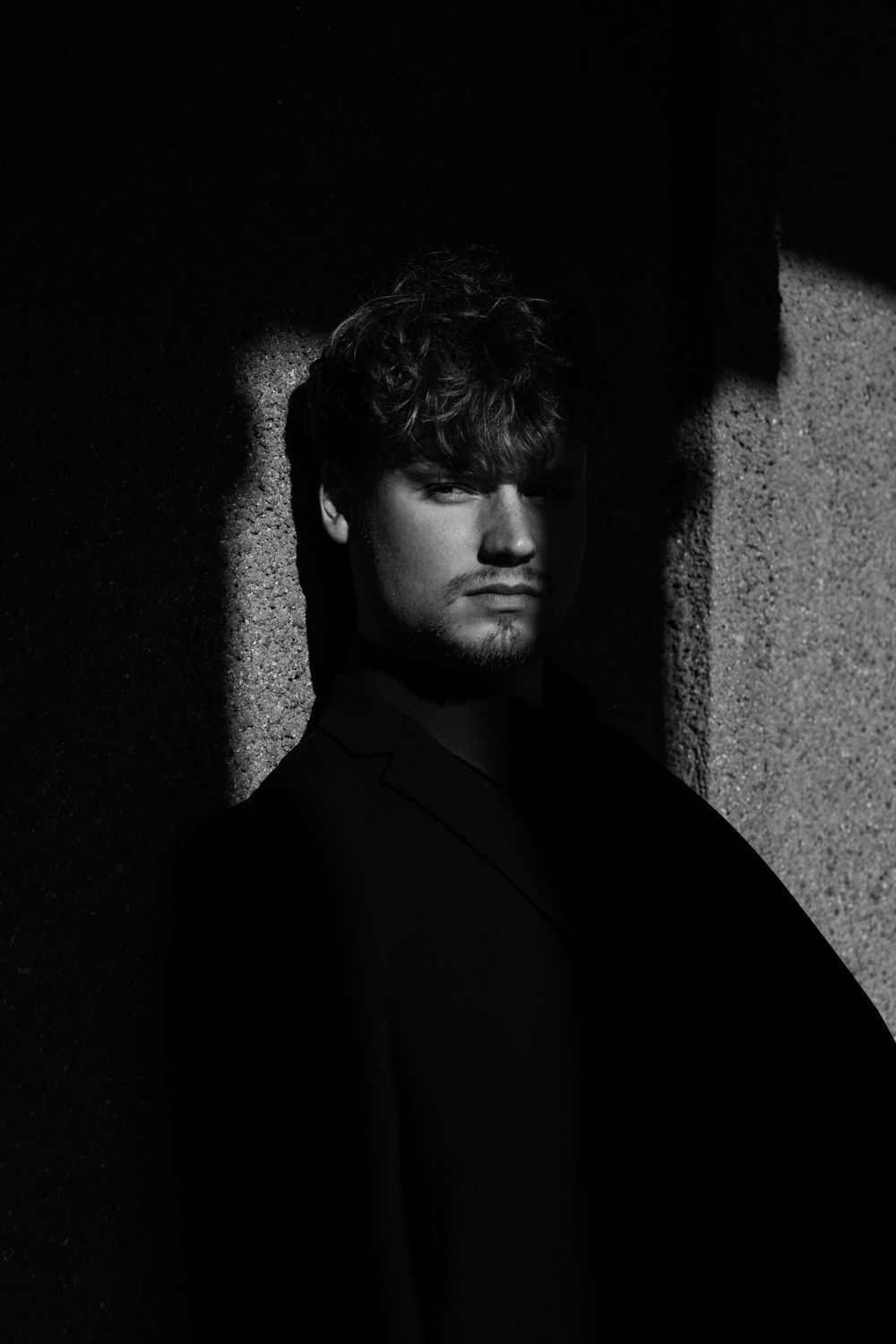 Moody black and white portrait with dramatic side lighting and deep shadows.