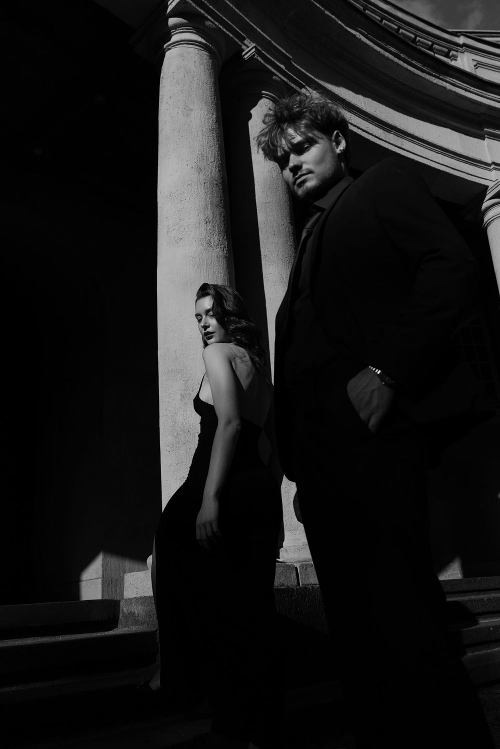 Dramatic architectural photograph with figures standing between classical columns in shadow.