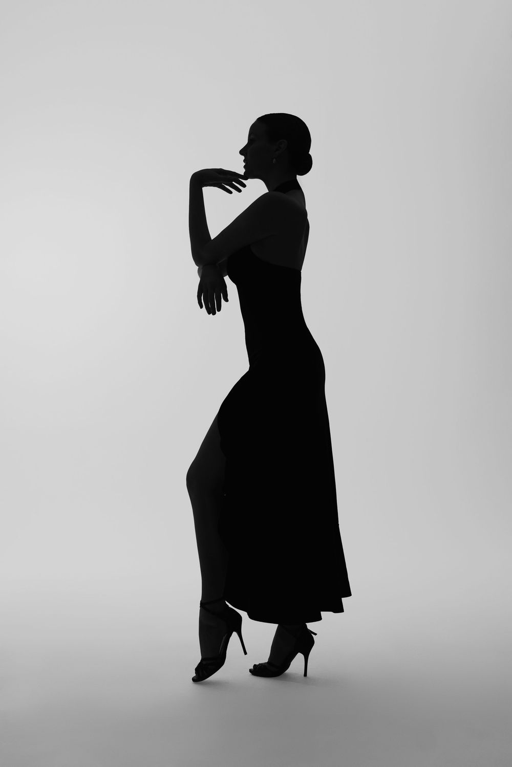 Elegant black silhouette of a woman in a long dress and heels posing gracefully against a light gray background.