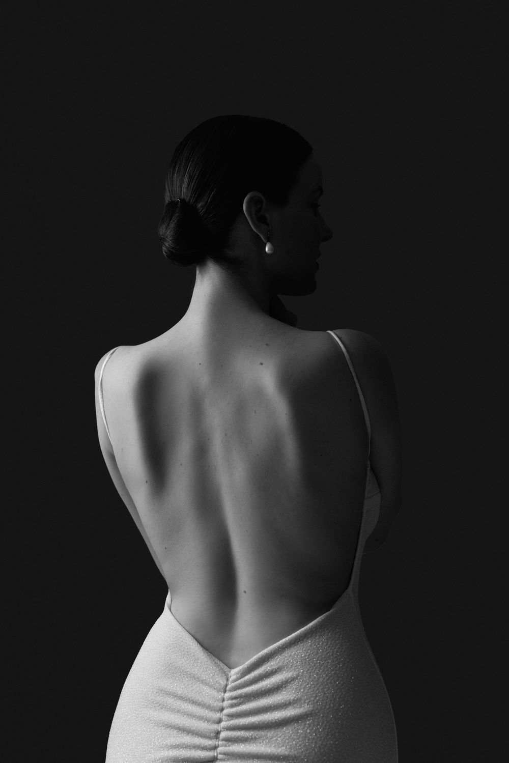 Black and white photo of a woman in a backless white dress, showcasing elegant back and pearl earring.
