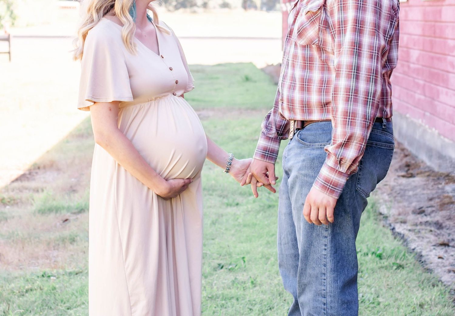 Rustic outdoor maternity photoshoot near pink barn walls in natural lighting.