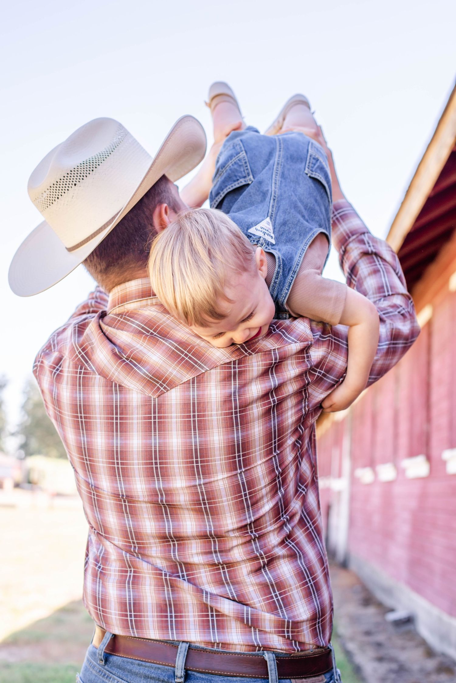 Sweet family embrace captured in golden light by red barn.