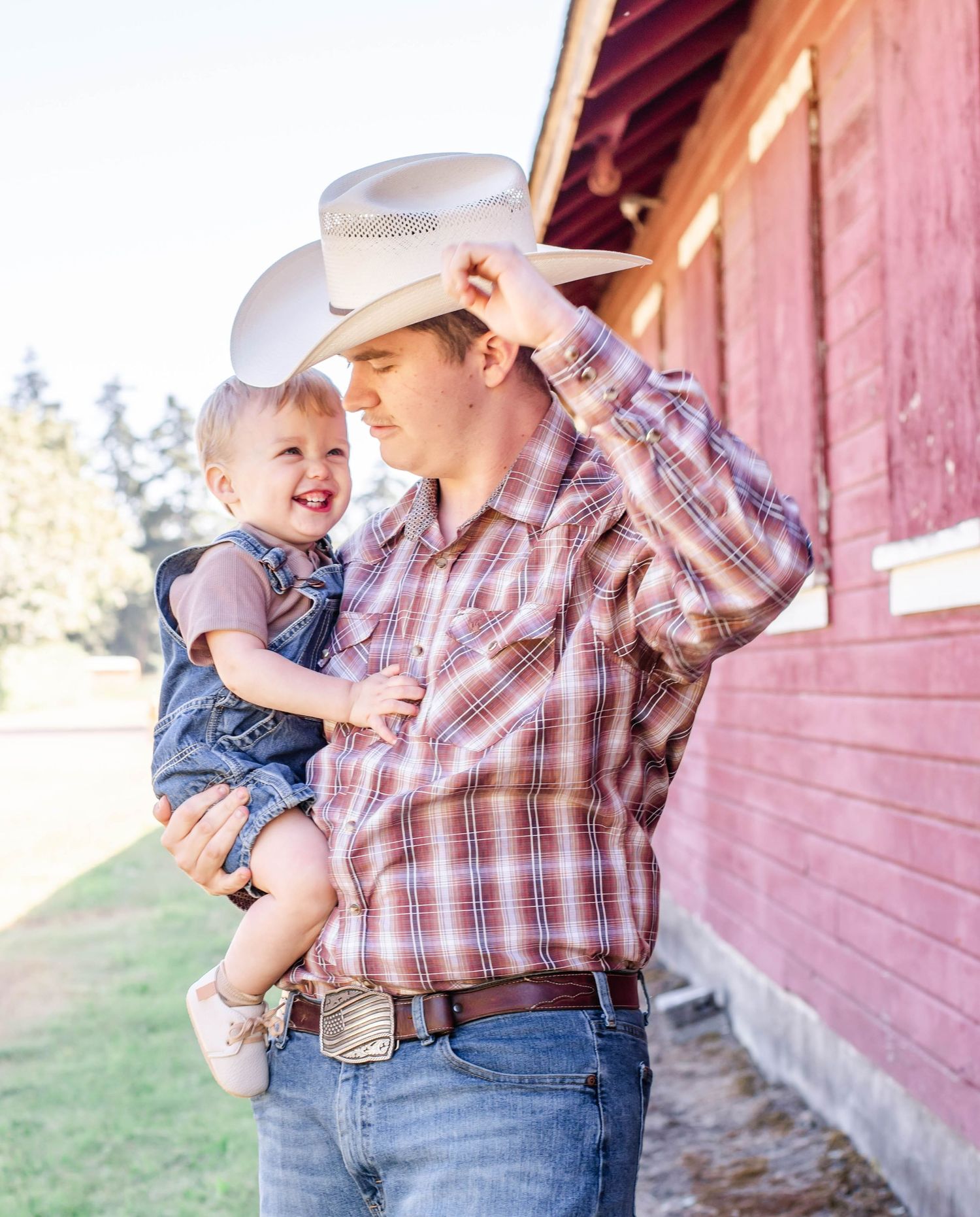 Playful family moment captured against rustic red barn backdrop.