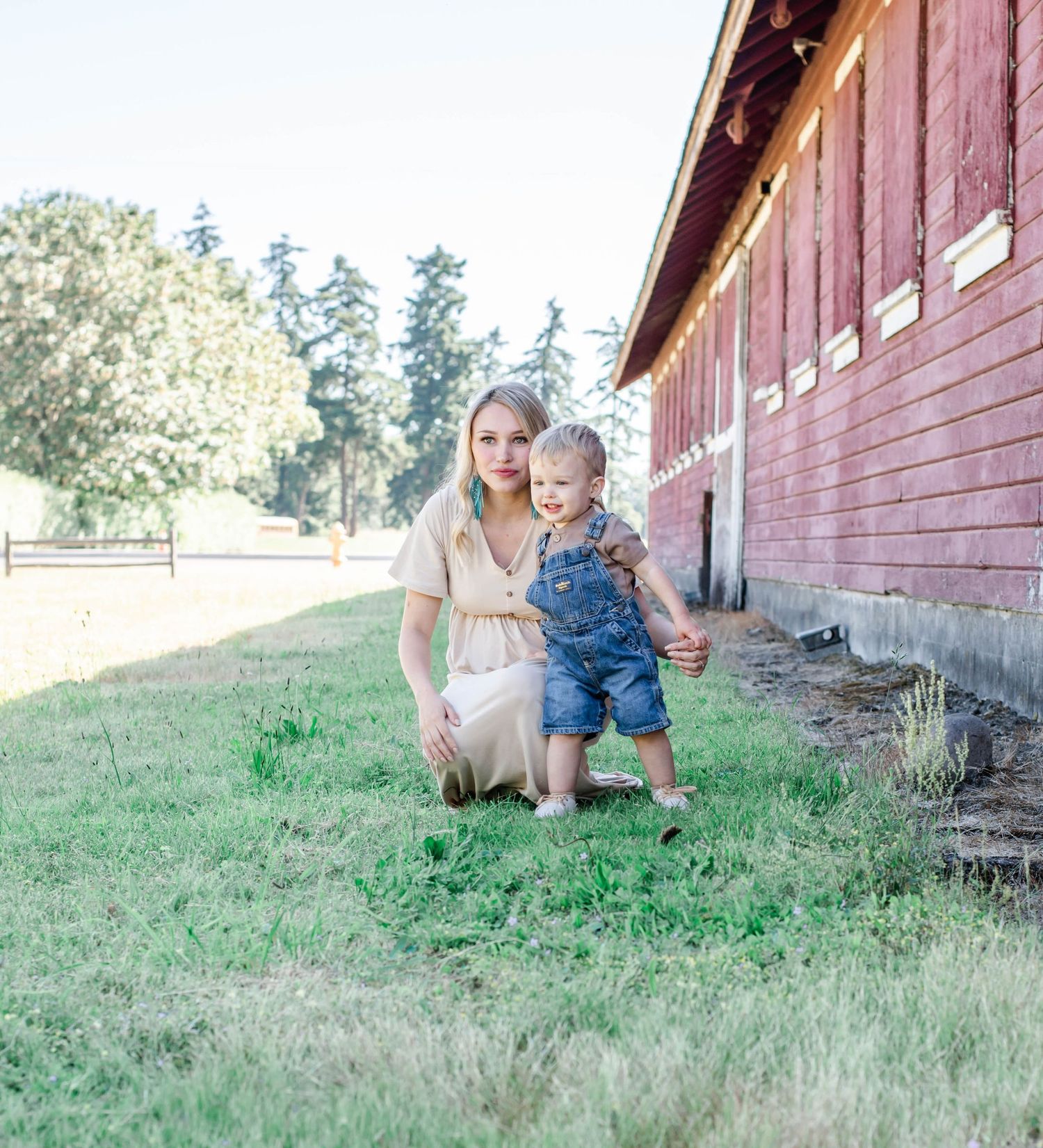 Casual family portraits on grassy hill beside vintage red barn structure.