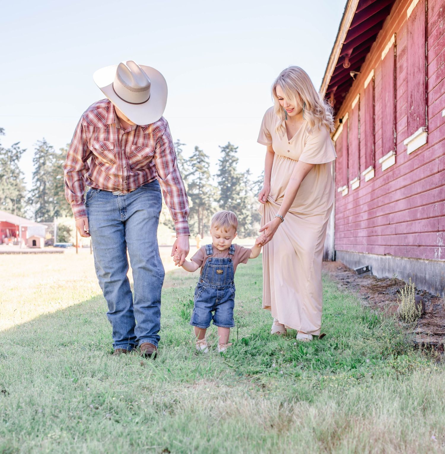 Family enjoying outdoor photoshoot by rustic red barn in countryside setting.