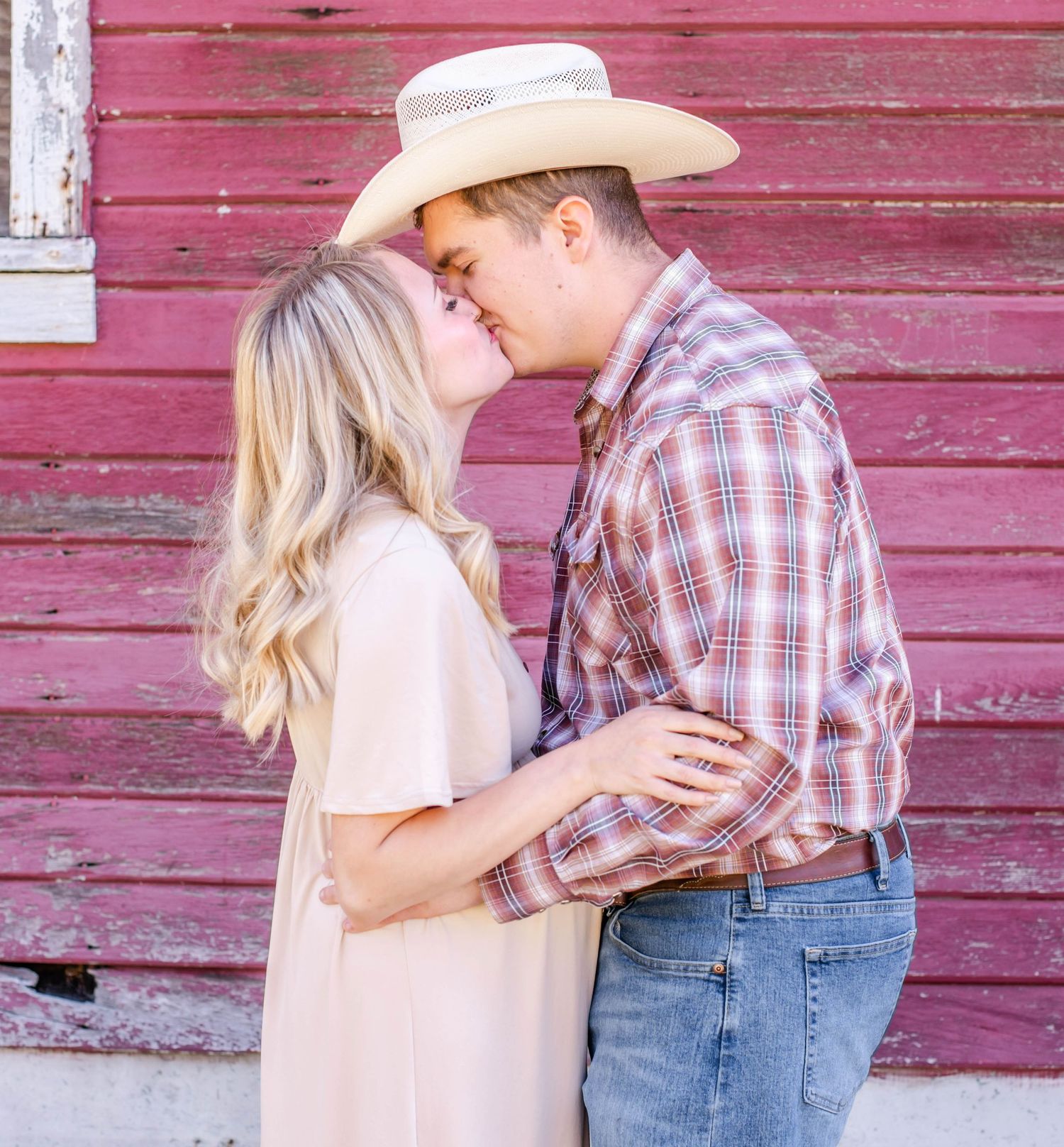 Intimate family moment captured against weathered red barn siding.
