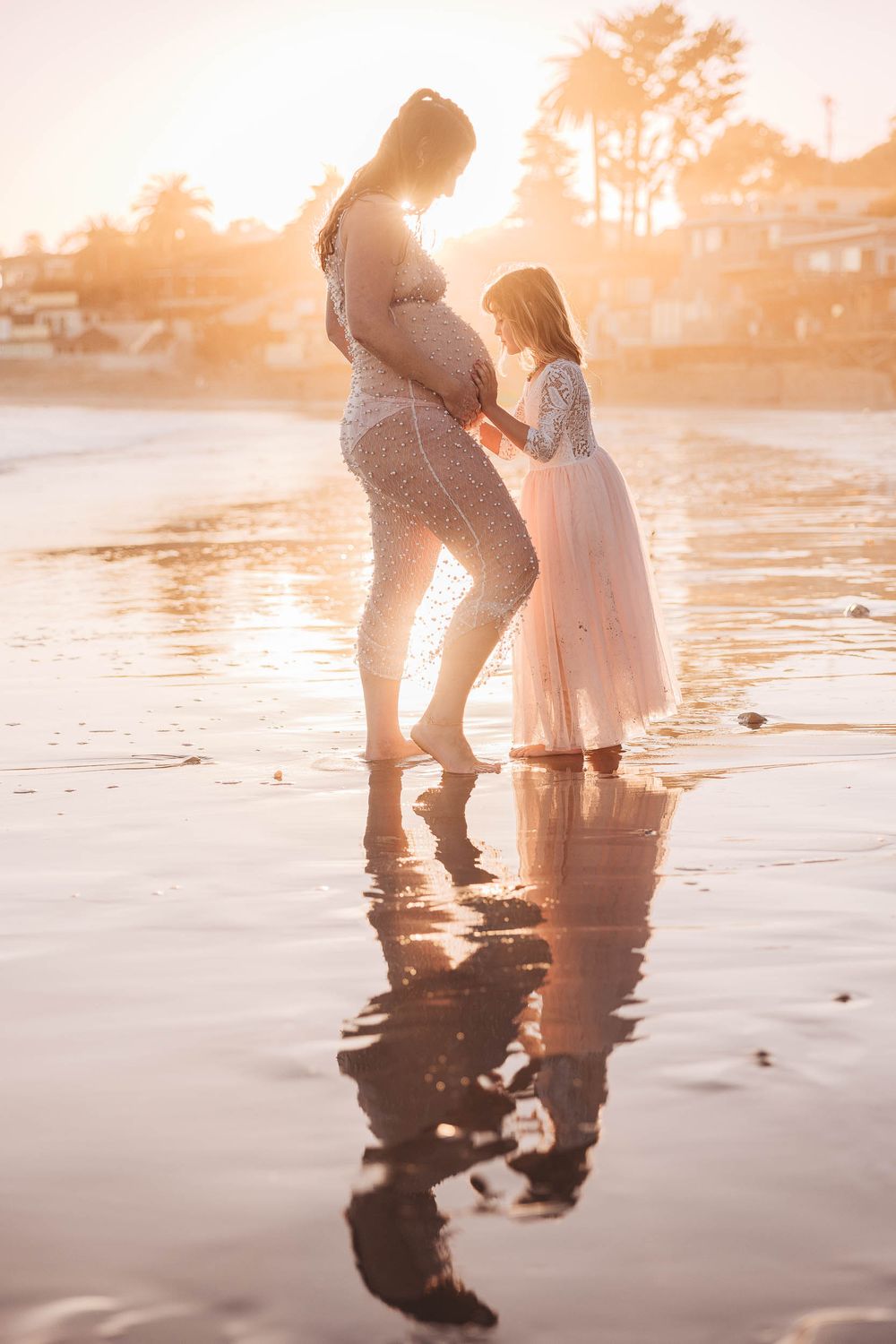 A tender sunset beach moment shows figures reflected in wet sand as golden light filters through palm trees.