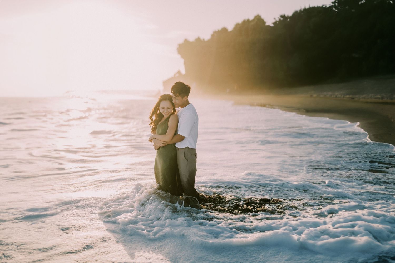 Couple embracing during sunset beach photoshoot with golden light and ocean waves.