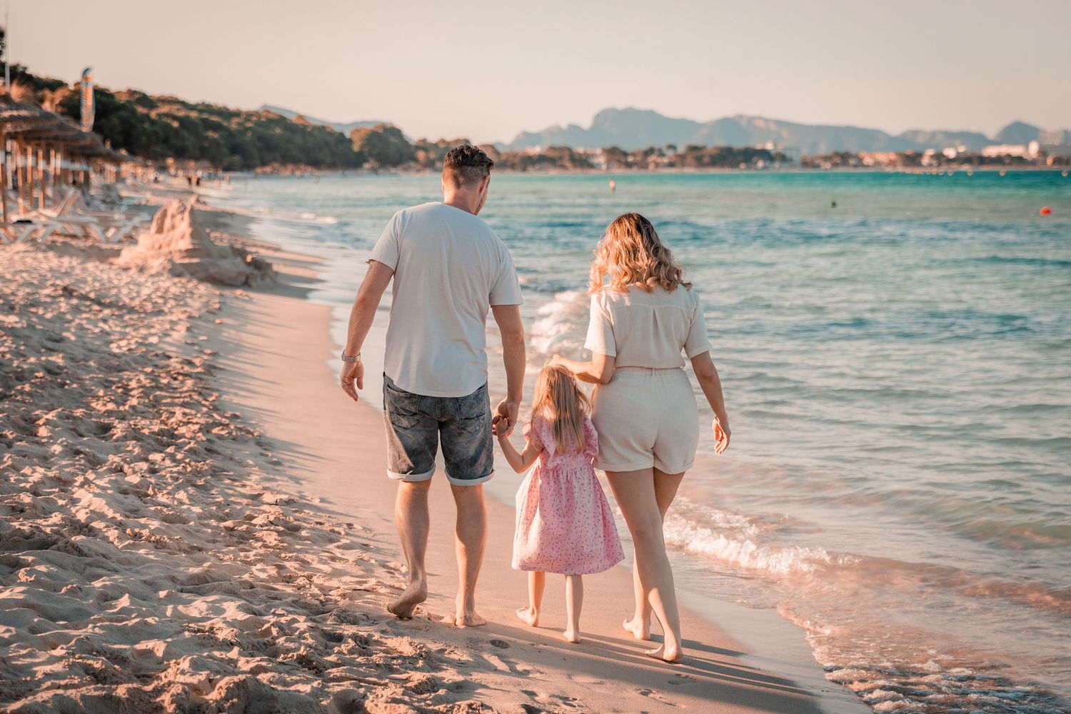 A family holding hands and walking along the shoreline during a casual lifestyle beach photo session in Mallorca.
