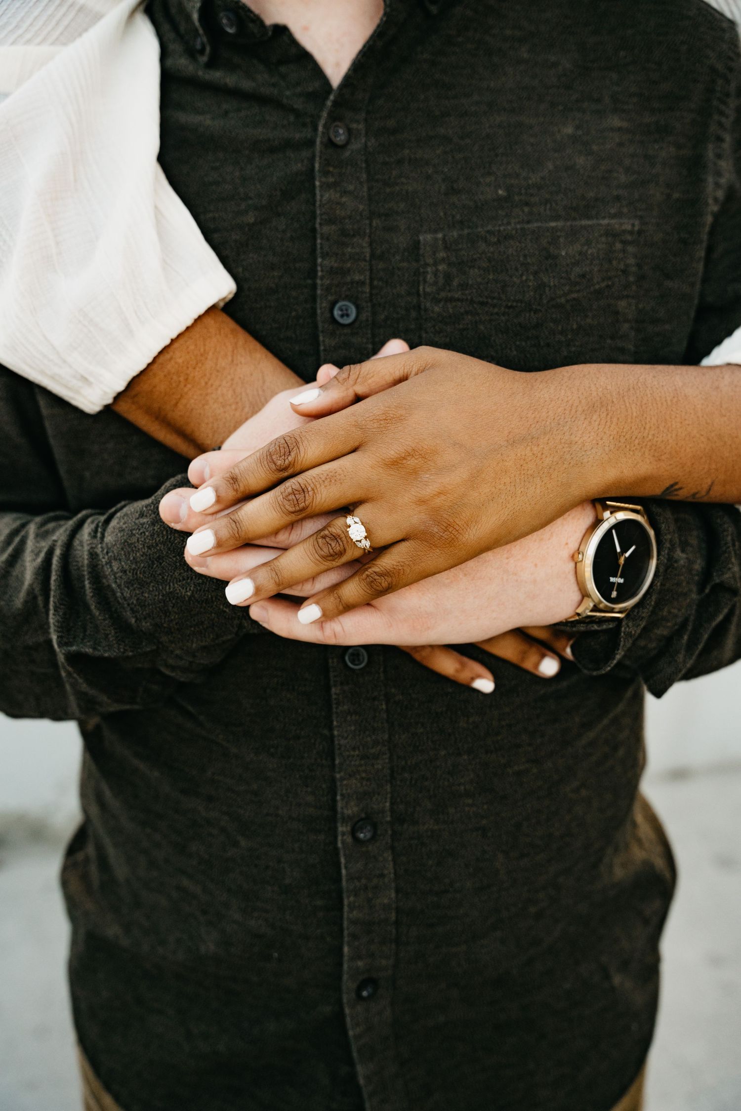Close-up of intertwined hands with engagement ring and watch details in downtown San Diego.