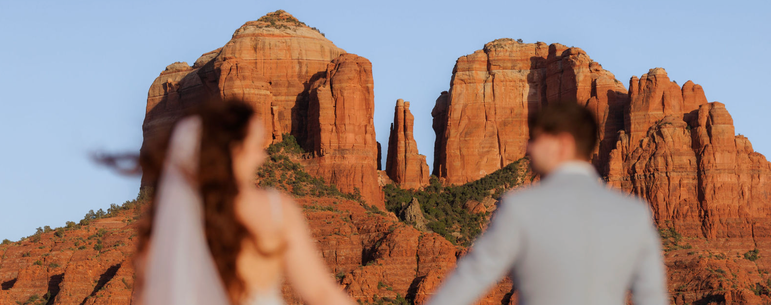 Couple holding hands facing Cathedral Rock formations at sunset in Sedona, Arizona.