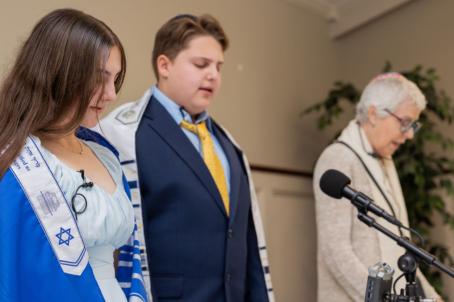 Three people stand at microphones during a religious ceremony.