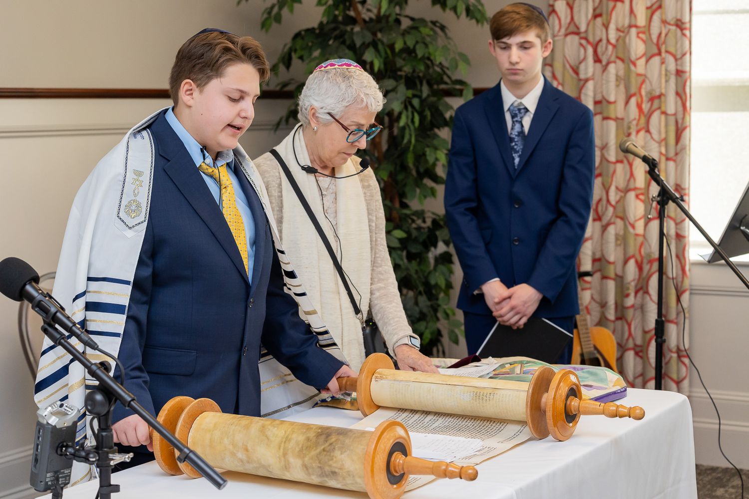 A bar mitzvah ceremony shows people gathered around the Torah scroll at a synagogue during the reading.