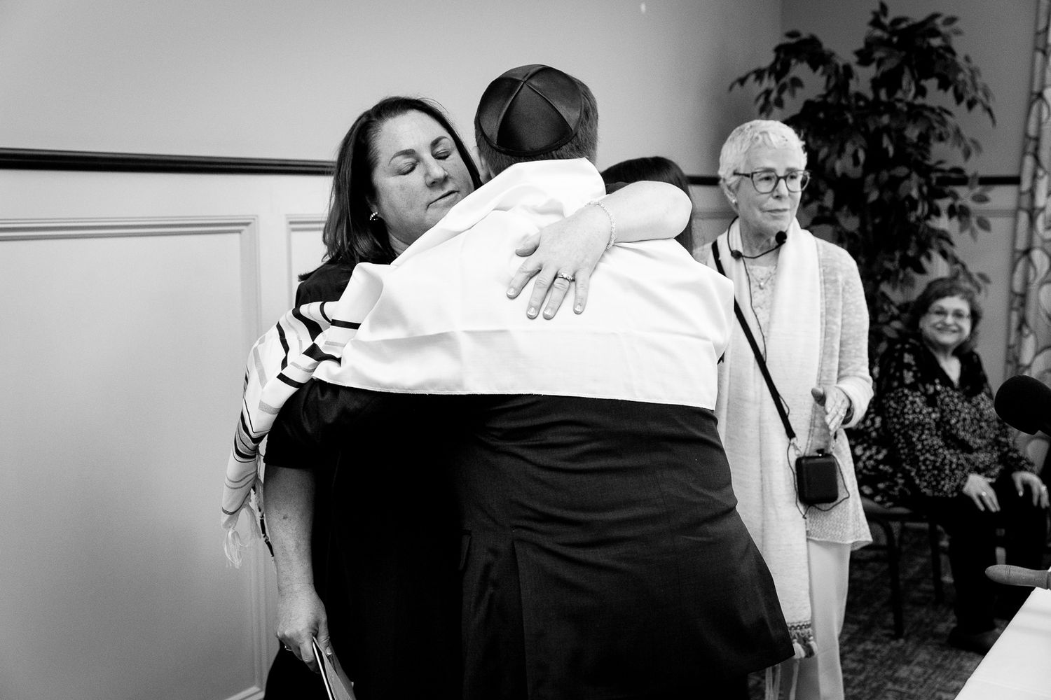 A black and white candid photo capturing an emotional embrace during a religious ceremony.