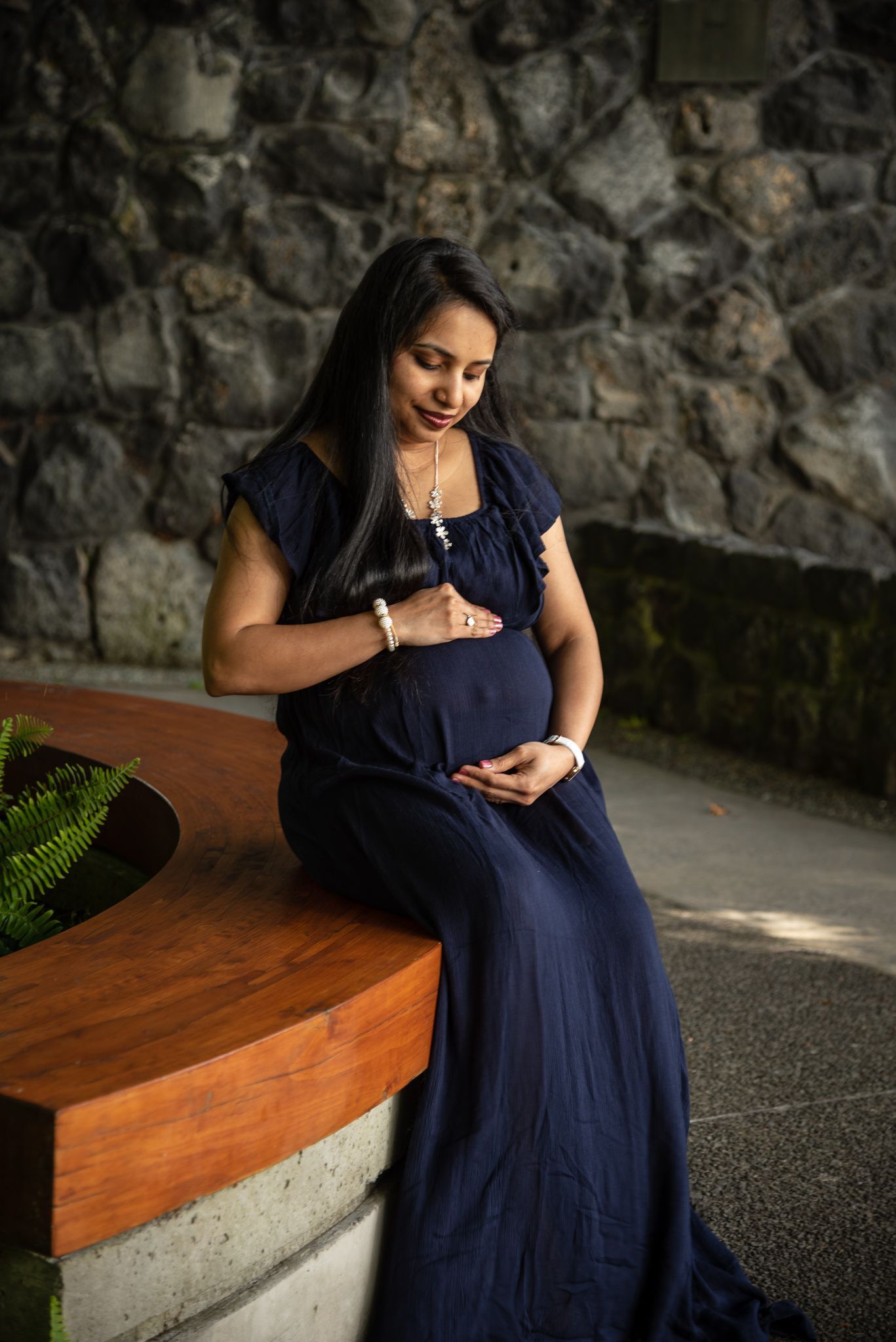 Figure in navy dress sitting in meditation pose against stone wall.