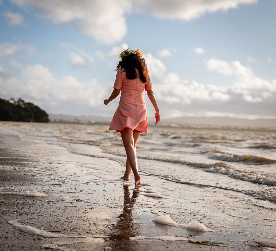 Person in pink dress running joyfully along beach shoreline at sunset.