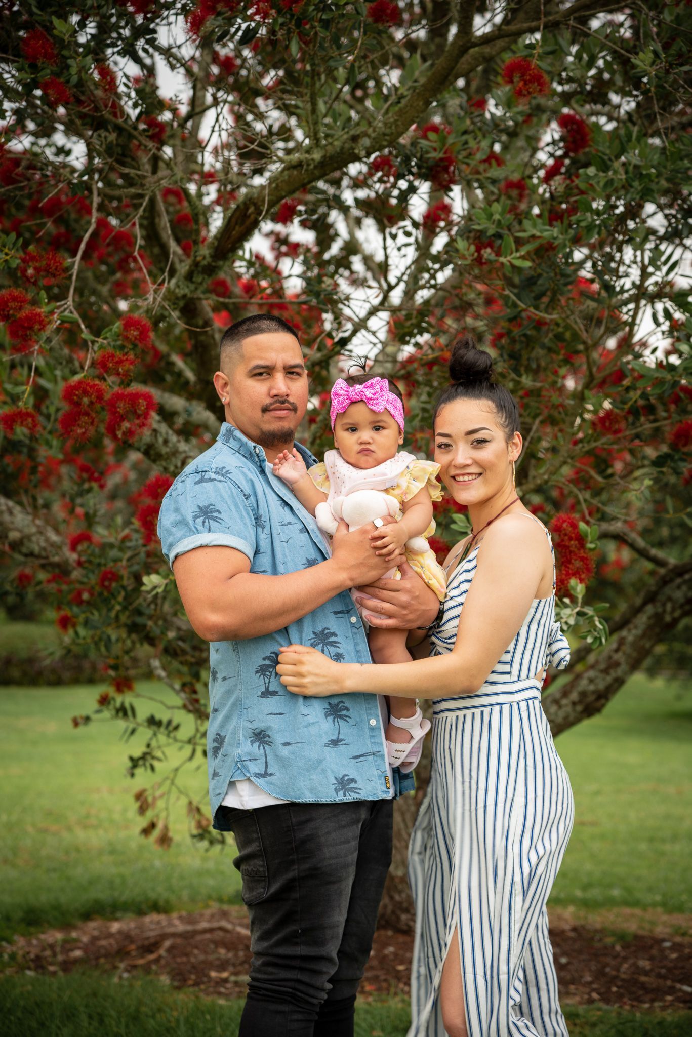 Family posing together under beautiful red flowering tree in garden setting.