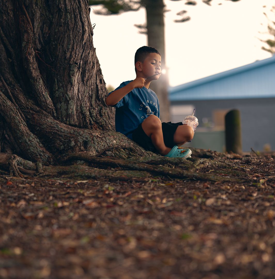 Child sitting peacefully against large tree trunk in golden sunlight.