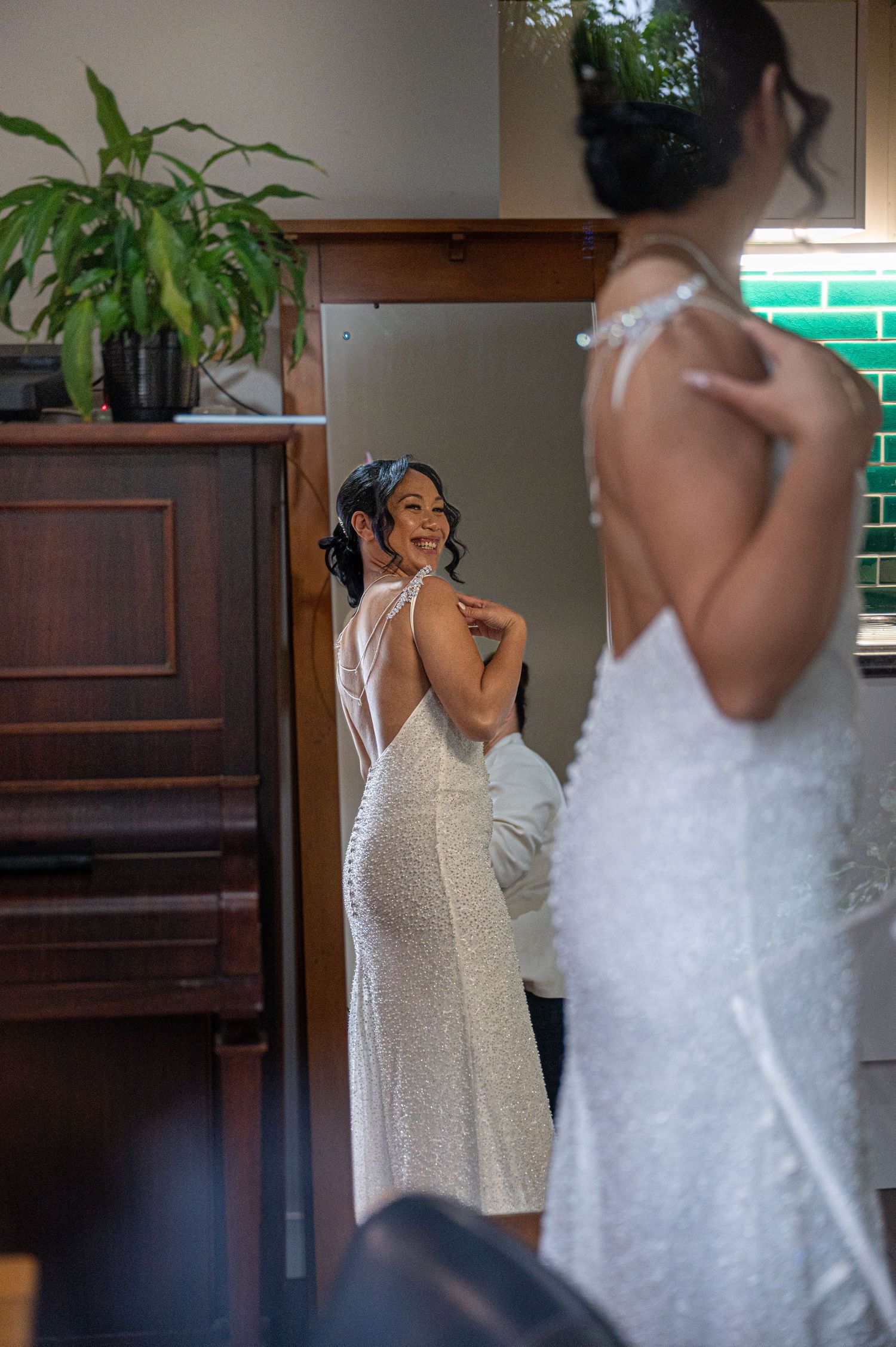 A woman in a sparkly white dress admires herself in a mirror while getting ready.