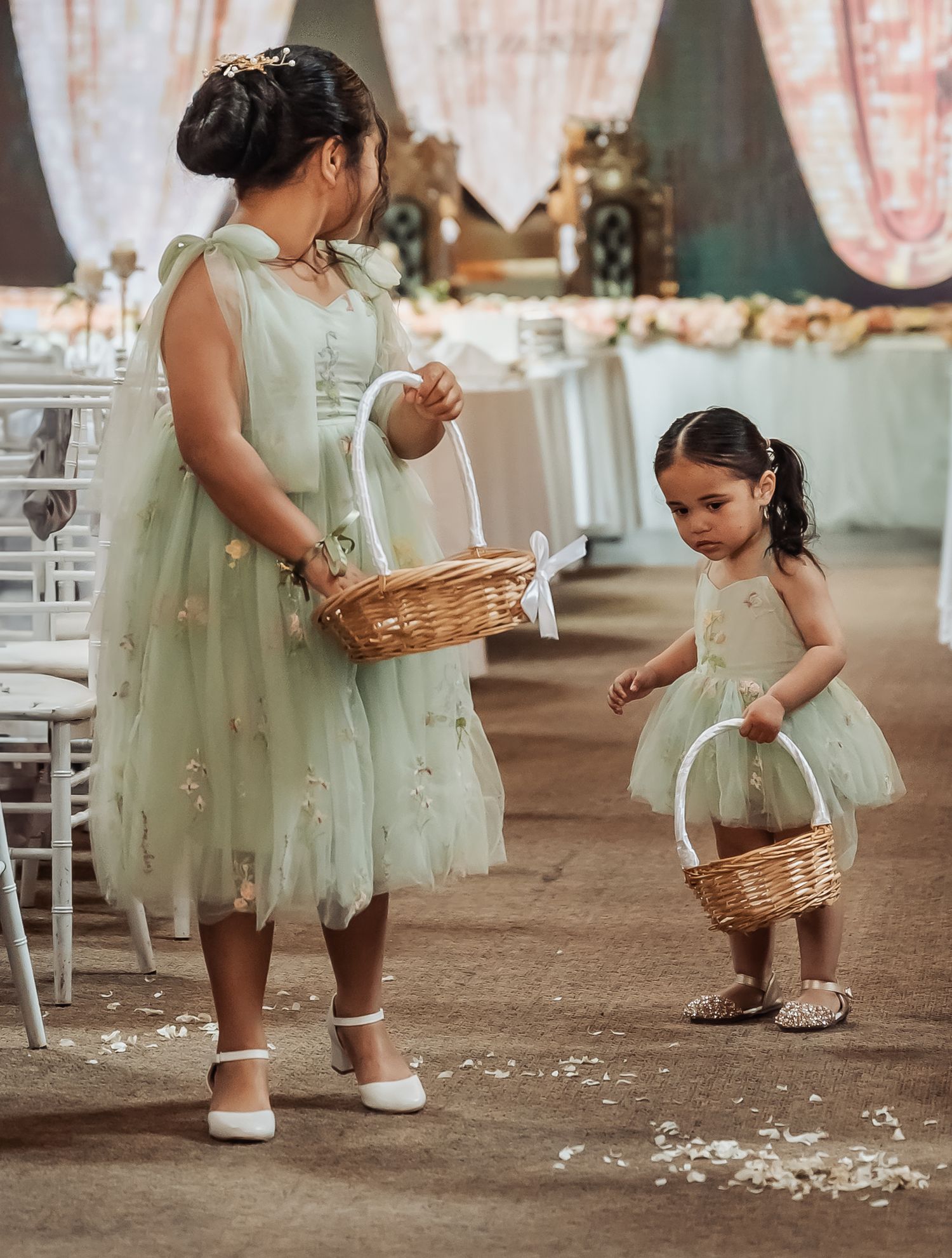 Two figures in matching mint green tulle dresses hold flower baskets at an elegant wedding reception setting.