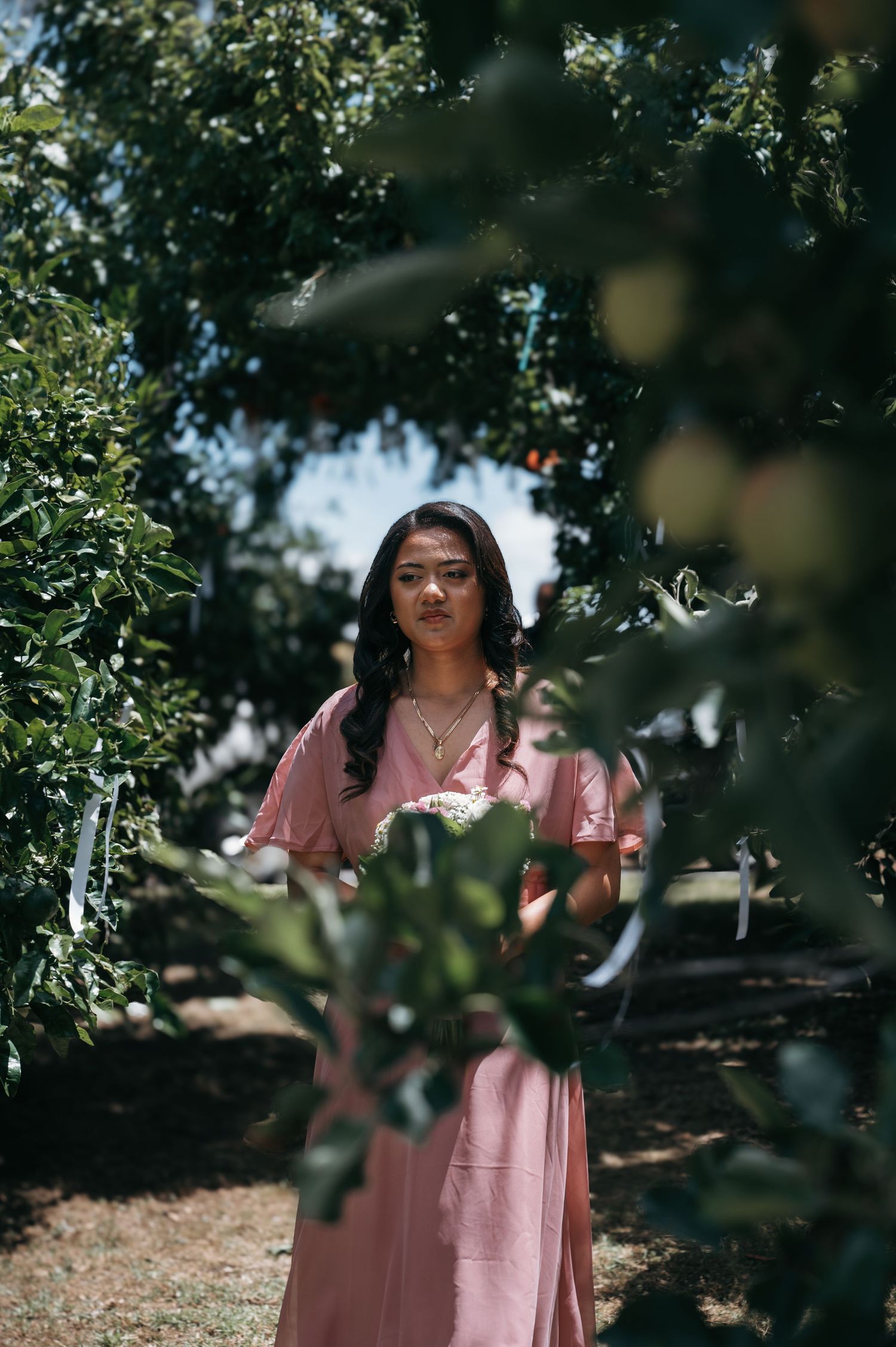 A person in a pink dress stands among green foliage on a sunny day with dreamy bokeh lighting effects.