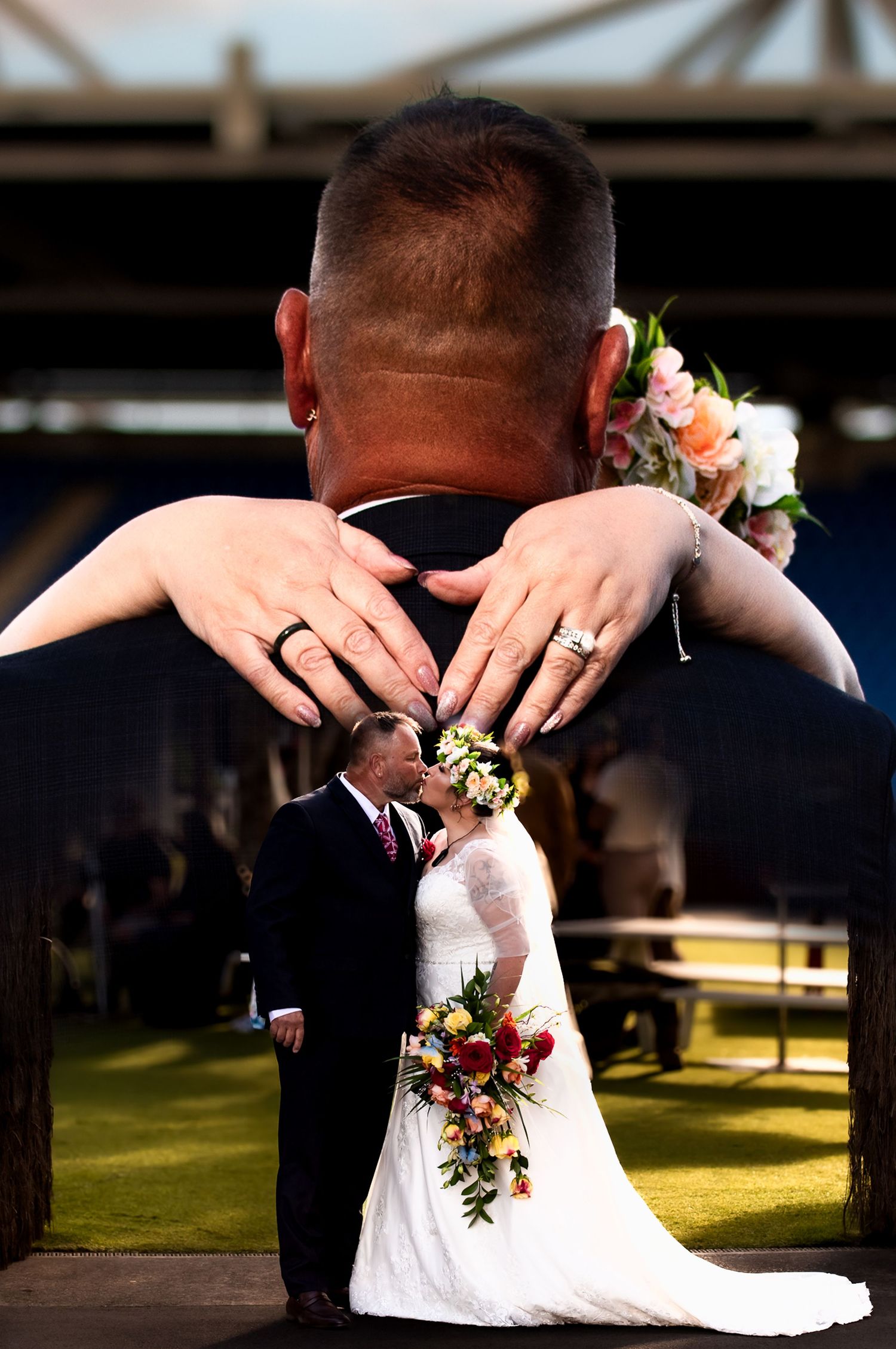 Creative wedding photo showing hands forming a heart shape around a couple during an outdoor ceremony.