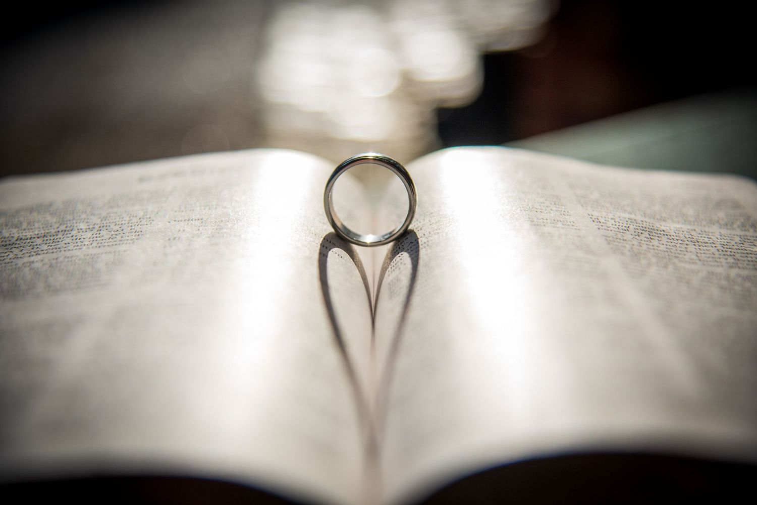 Wedding ring casting heart shadow on open book pages in artistic macro shot.